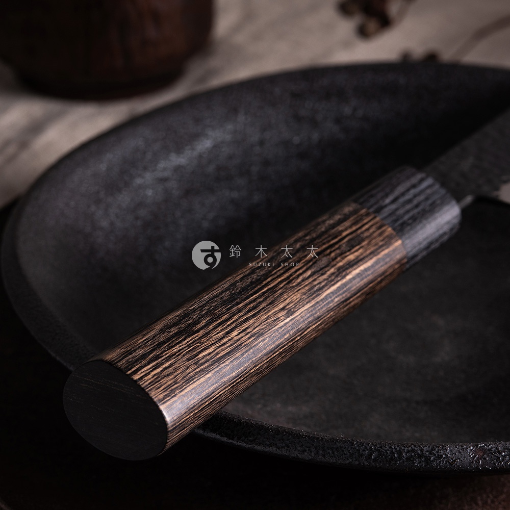 玄 / Chef's knife 主廚刀24cm，刀柄為深棕色木紋材質，搭配黑色金屬刀身，置於黑色紋理的圓盤上。