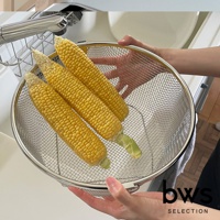 不鏽鋼圓形瀝水籃內盛著三根新鮮玉米，籃子採用細密網格設計，邊緣為銀色不鏽鋼材質，由雙手拿握，展示其瀝水功能。
