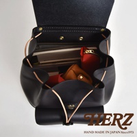 黑色職人手作皮革後背包，內部裝有書籍、紅色零錢包及棕色皮夾。包包以抽繩閉合，並有金屬鎖扣。