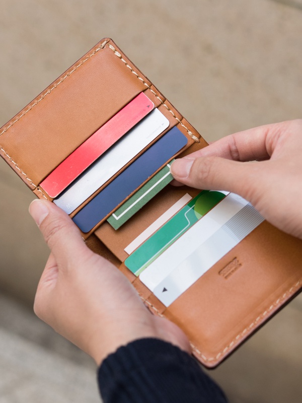 皮革二折直式短夾，淺棕色皮革，內有卡片槽，展示多張信用卡、會員卡等，部分卡片為紅色、藍色、白色及綠色條紋。