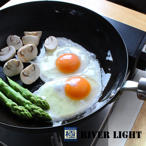 黑色金屬平底鍋中烹調著兩顆煎蛋，旁邊擺放著切片的蘑菇和綠色的蘆筍。
