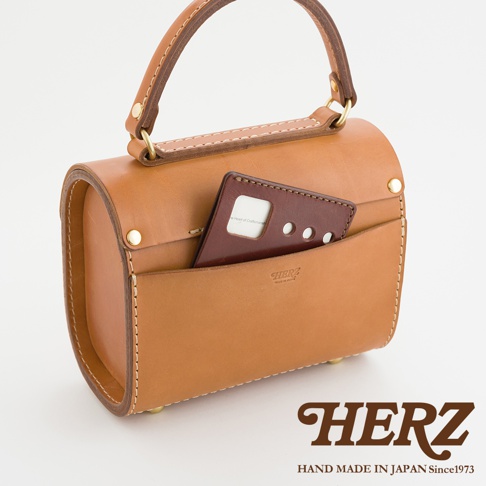 職人手作皮革復古杜勒斯手提包，採用鞣製的棕褐色皮革製成，設有頂部提把、前置口袋，並裝有深棕色皮革配件。包包以手工縫線和金色五金件裝飾。