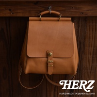 職人手作皮革後背包，呈現自然棕色，採用皮革材質，配有金屬釦環與可調節背帶，設計簡約，適合日常攜帶。