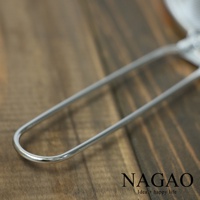 不鏽鋼材質的濾茶器，銀色金屬光澤，帶有U形把手，置於木紋背景上。