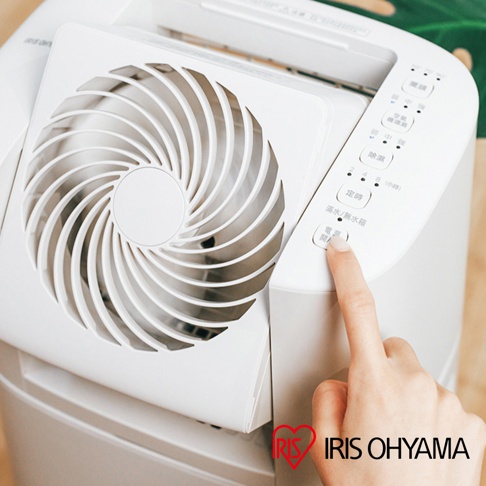 白色IRIS OHYAMA乾燥循環除濕機DDC-60，近拍機身側面，手指正按下電源按鈕，上方可見風扇和控制面板。