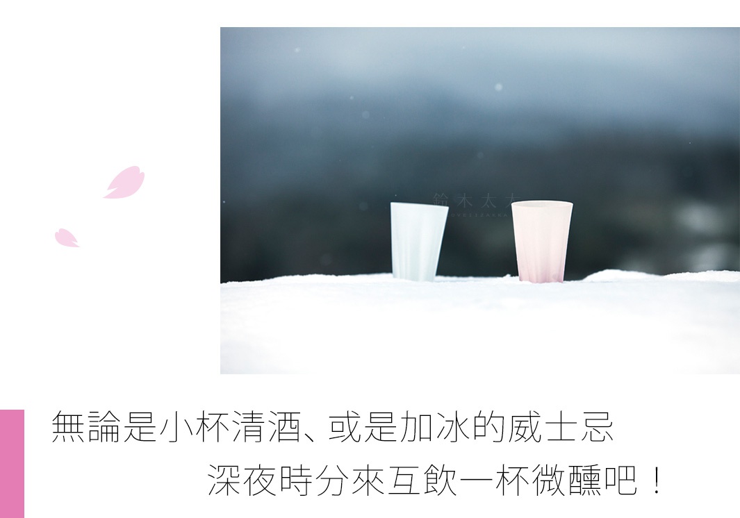 兩個透明玻璃杯，一個淺藍色，一個淺粉色，放置於雪地中，背景為模糊的深色調。