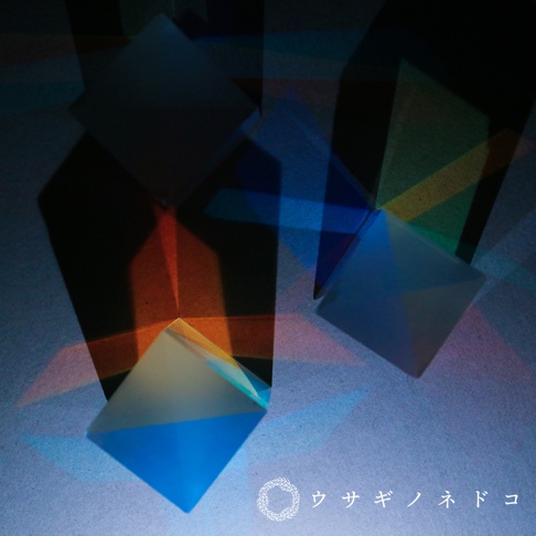 透明稜鏡立方塊在藍色、橙色和黃色的光線下呈現出多面體反射，部分立方塊帶有漸層藍色和白色，與背景的陰影形成對比。