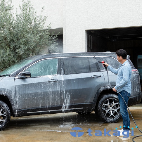 男人正在用水槍清洗一輛 SUV，車身佈滿泡沫。