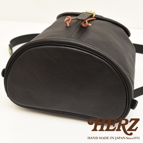 職人手作黑色皮革單扣束口後背包，圓潤底部，頂部束繩設計，搭配金屬釦環。