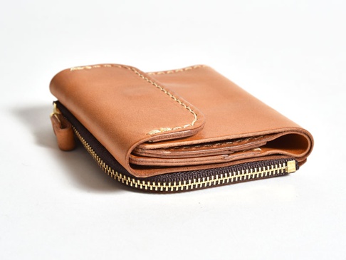 淺棕色皮革製成的手工方形短夾，帶有拉鍊開合和翻蓋設計，縫線清晰可見。