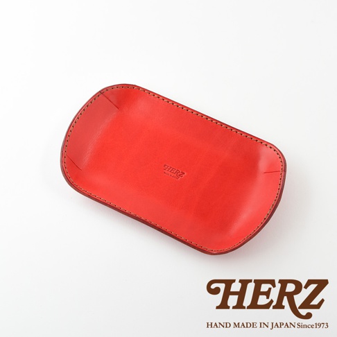 職人手作紅色皮革小物收納盤，表面壓印有「HERZ MADE IN JAPAN」字樣，邊緣以車縫線裝飾，呈現簡約實用的設計。