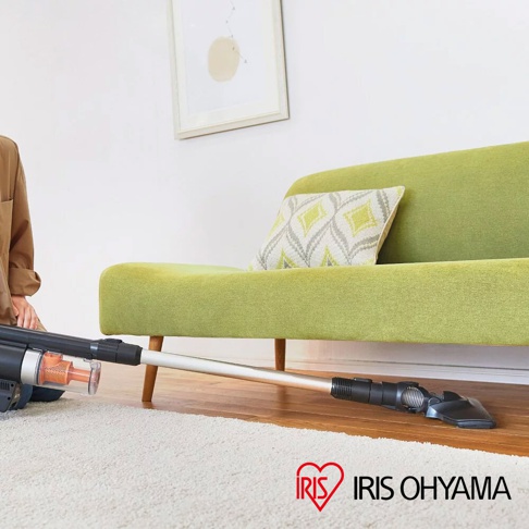 氣旋式超輕量無線手持吸塵器 SCD-140，銀色金屬管身與黑色機身，搭配透明集塵筒，正在地板上進行清潔，後方有綠色沙發與抱枕。