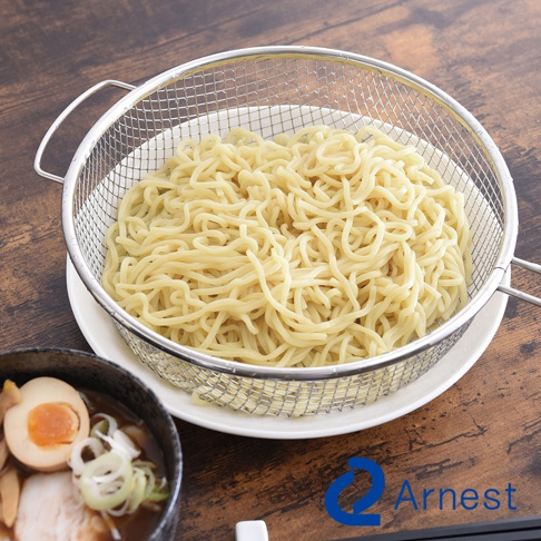 銀色不鏽鋼手持料理濾網，網狀結構，裝有煮熟的黃色麵條，置於白色盤子上。