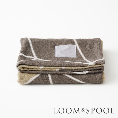 摺疊的咖啡色毛巾，上面印有白色幾何圖案，並有一個空白的淺色標籤。