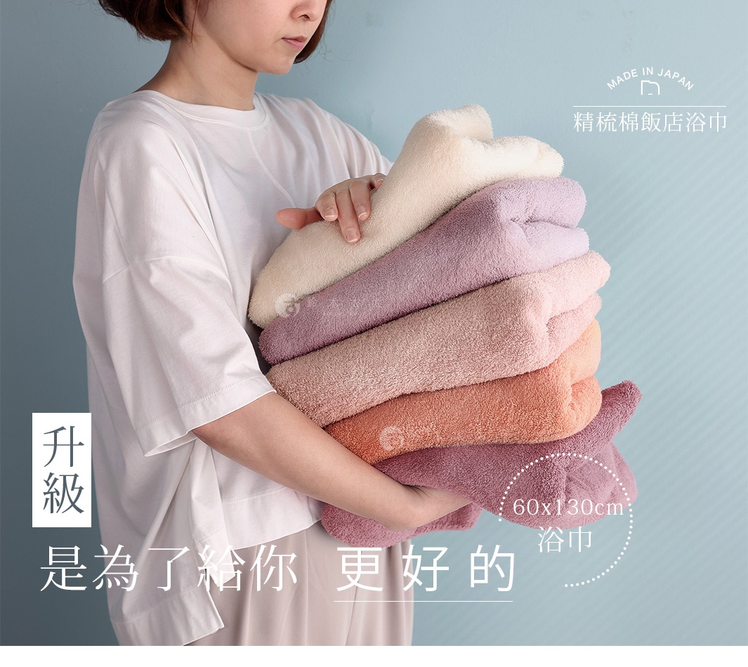 一位短髮女性穿著白色上衣，雙手懷抱著一疊色彩柔和且質感蓬鬆的日本桃雪精梳棉飯店浴巾，浴巾由米白、淺紫、粉紅、橘紅與深紫色組成，圖片右上角標示日本製造與精梳棉飯店浴巾字樣，下方則標註尺寸為六十乘以一百三十公分。