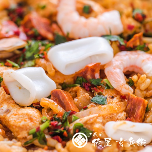 近距離特寫，顯示一盤海鮮飯，有鮮蝦、白色花枝圈、香腸塊，搭配米飯和綠色香草。