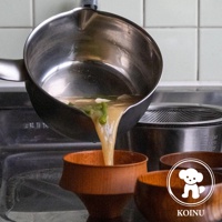 三層不鏽鋼雪平鍋傾斜，鍋內湯汁正倒入木碗中。鍋身為銀色不鏽鋼材質，外側為黑色塗層，鍋緣有導流設計。背景為廚房環境，可見濾網和瓷磚牆面。