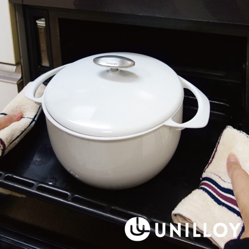 白色琺瑯鑄鐵鍋，配有銀色圓形鍋蓋把手，鍋身兩側有弧形提把，鍋具置於烤箱烤架上，兩側有條紋布巾。