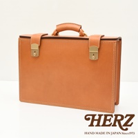 職人手作的酒紅色皮革機師箱，配有金色鎖扣和提把，箱體邊緣縫線明顯。