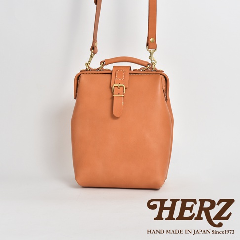 職人手作皮革迷你軟皮杜勒斯包，採用柔軟的天然皮革製成，呈現溫暖的棕褐色。包款設計經典，配有金色搭扣和可調節的肩帶。