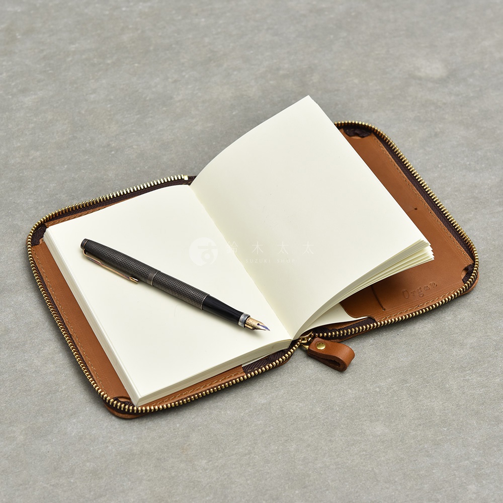 一個打開的棕色皮革記事本收納包，裡面放著一本空白筆記本和一支鋼筆。