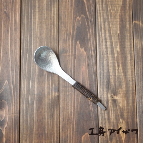 銀色鋁製湯勺，勺面有錘目紋，勺柄部分纏繞著深棕色編織物。