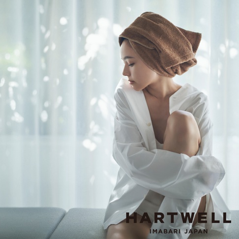 一名女子頭裹棕色毛巾，身穿白色寬鬆襯衫，坐在沙發上。