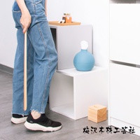 加長檜木鞋拔，末端有一個弧形握柄，整體為原木色。旁邊擺放著一個藍色圓形衛生紙盒和一個木製面紙盒。