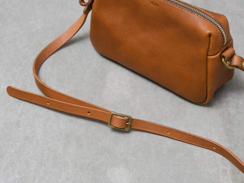 職人手作皮革Organ輕巧拉鍊單肩包 (G-80) M，採用天然棕色皮革製成，帶有可調節長度的細皮革肩帶及黃銅金屬扣。包身呈現簡潔的長方形設計，頂部有拉鍊開合。