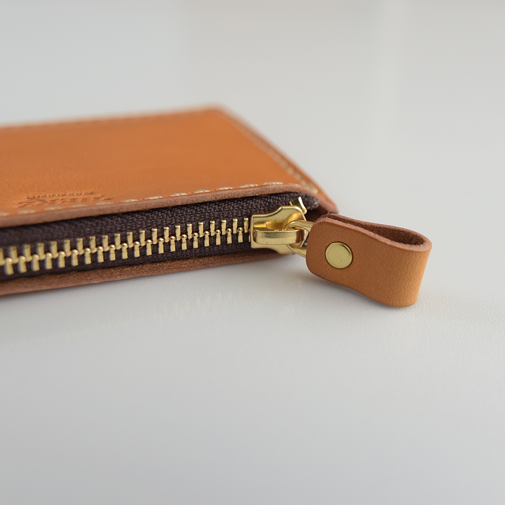 淺棕色皮革L型拉鍊迷你短夾，帶有金色拉鍊頭和同色系皮革拉環，以細緻的縫線手工製作。