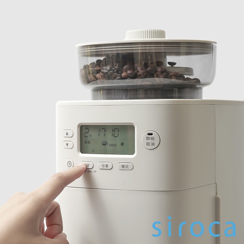 淺灰色 SC-C2510 石臼式全自動研磨咖啡機，上方透明研磨槽裝有咖啡豆，下方主機面板顯示時間、溫度、容量和模式按鈕，手指正按下「研磨」按鈕。