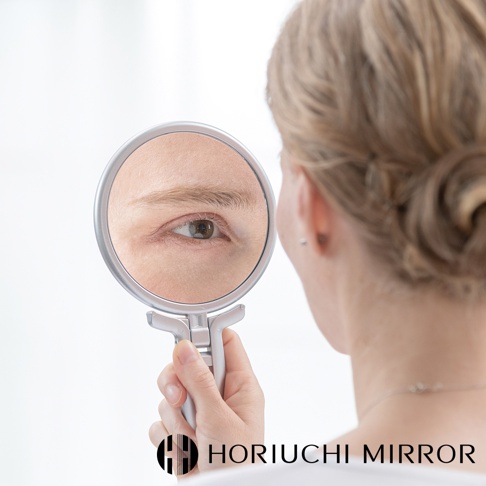 堀內鏡 HORIUCHI MIRROR 品牌標誌下方，一名女子正拿著手持鏡，鏡中映照出她的眼睛特寫。
