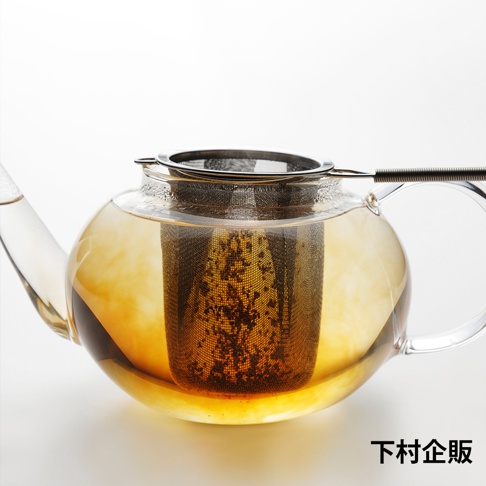 透明玻璃茶壺內，裝有琥珀色茶湯，壺中置有一個不鏽鋼濾網，網內有茶葉沉澱，濾網外圍有細密網孔，濾網頂部有金屬邊框及手柄。