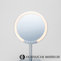 銀色圓形LED化妝鏡，鏡框周圍有暖白色LED燈光，鏡面下方有三個控制按鈕，產品立於銀色支架上，背景為淺灰色。