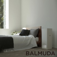 The Pure 空氣清淨機，白色直立式機身，簡約設計，放置於木製床架旁，搭配白色床單、灰色枕頭與深灰色毛毯，窗外綠意透入。