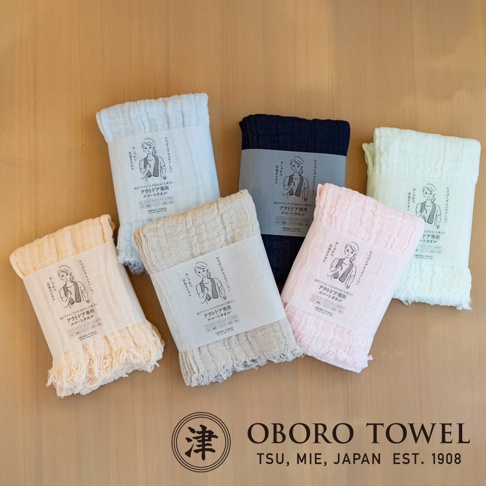 六條三層紗純棉輕柔戶外掛脖毛巾，顏色包含淺藍、深藍、米白、米黃、淺粉紅，材質輕薄，帶有流蘇邊緣，每條毛巾皆附有產品標籤。