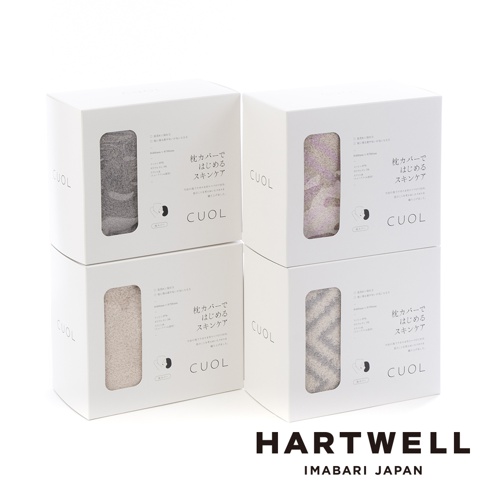 四個白色方形紙盒堆疊展示，每個紙盒的透明窗口中可見不同顏色的CUOL今治柔彈伸縮美肌枕套，分別為灰色、粉紫色、米白色及灰白色相間條紋。