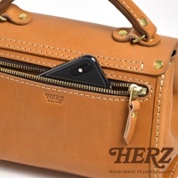 職人手作皮革迷你手提包，顏色為棕褐色。包包採用厚實皮革製成，縫線精緻，帶有拉鍊前袋，可放入手機。包包配有提把和金屬扣環，質感扎實。