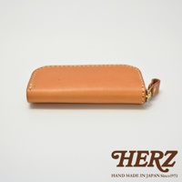 HERZ 品牌標誌，下方為 HAND MADE IN JAPAN Since1973 字樣，旁邊是一個棕色皮革製的橢圓形拉鍊鑰匙包。
