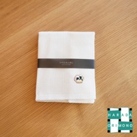 一條白色八重紗精繡萬用吸水擦拭巾，帶有深灰色包裝帶，上面印有日文和英文品牌名稱。擦拭巾右下角繡有可愛的日式壽司圖案。