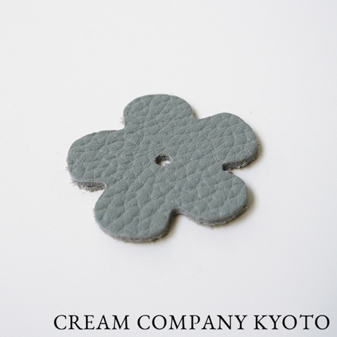 淺灰色皮革製成的五瓣花形飾品，表面有細緻紋理，中央有一個小孔，是京都職人手作半月迷你手提包的配件。