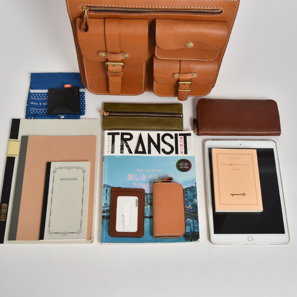 皮革三口袋三用後背包，附有兩組金屬釦，搭配一個藍色印花布、一個黑色零錢包、一個綠色長夾、一個棕色長夾、一本筆記本、一本雜誌、一個證件套、一個鑰匙包及一台平板電腦。
