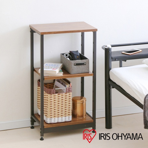 三層窄型層架，木紋層板搭配黑色金屬支架，層架上擺放書籍、收納籃、金屬罐和手機。