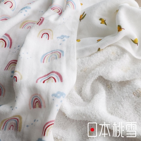 一面印有彩虹圖案的白色紗布方巾，旁邊疊著一條觸感蓬鬆的白色毛巾，毛巾上有著小黃花的圖案，右下角有「日本桃雪」的文字標記。