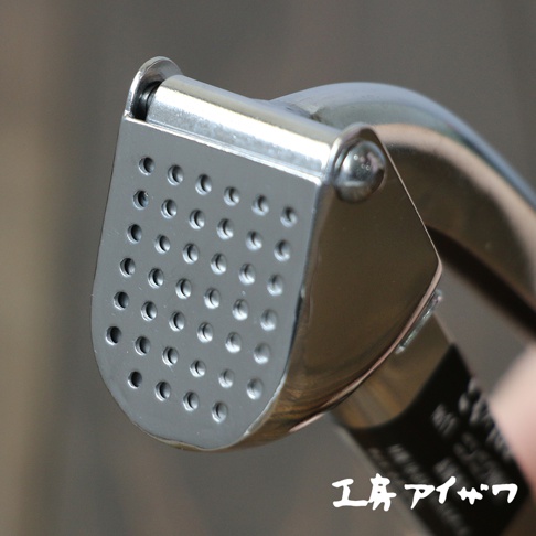 不鏽鋼壓蒜器，設有圓形壓孔的銀色金屬頭部，以及光滑的銀色手柄。