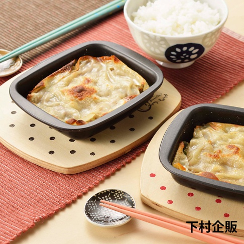 兩個黑色的迷你方形烤盤，裝有烘烤過的點心，放在木質隔熱墊上，墊上有圓點圖案。旁邊有一碗白飯、一雙筷子及一個小碟。