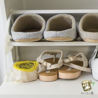 白色鞋架上展示著三雙藍白條紋室內拖鞋，以及一雙米白色編織涼鞋，旁邊還有一個黃色包裝的圓形物體。