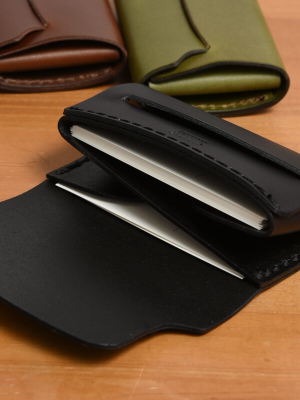 職人手作皮革迷你卡片收納夾 (KV-2)，黑色皮革製成，可收納多張卡片，設計簡潔，質感細膩。背景為木質桌面，並有棕色和軍綠色同款收納夾。
