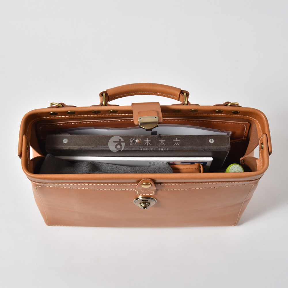 職人手作皮革軟式杜勒斯三用背包，淺棕色皮革，包身結構方正，頂部有提把、金屬扣環及磁扣，內部空間可見書籍、文件及小物件，整體展現復古與專業質感。