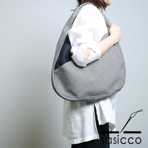 一位女士斜挎著一個三河木綿刺子織半月包，包身以黑白格紋圖案為主，一側點綴有黑色皮革拼接。